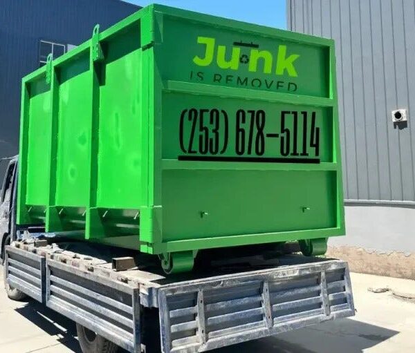 Bright green junk removal dumpster loaded on a flatbed truck outside a commercial building, showcasing professional junkisremoved services.